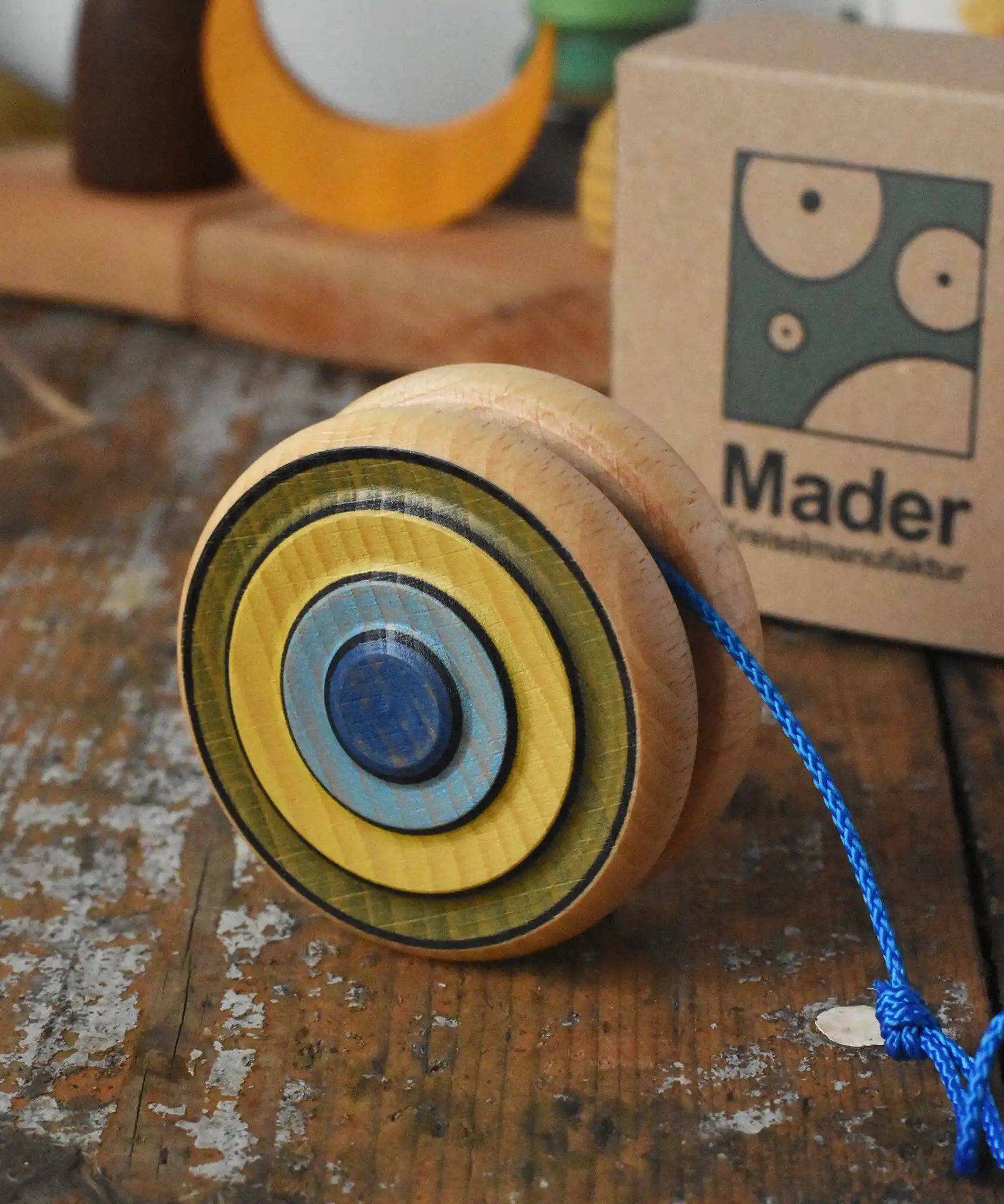 Mader Kreiselmanufaktur yoyo harlequin placed on a wooden desk in the Babipur playroom. The cardboard packaging box can be seen in the background.