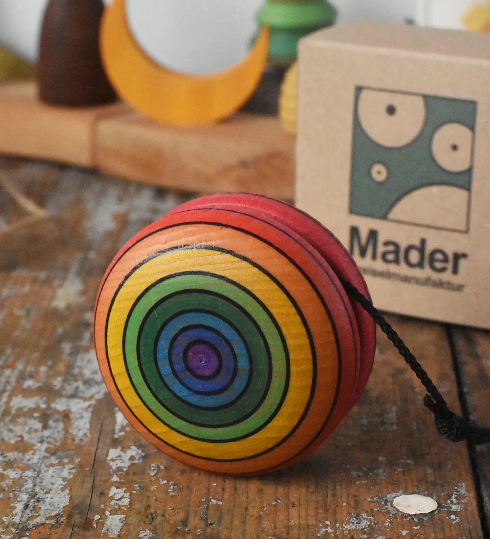 Mader yoyo rainbow placed on a wooden desk in the Babipur playroom. Cardboard packaging box can be seen in the background.