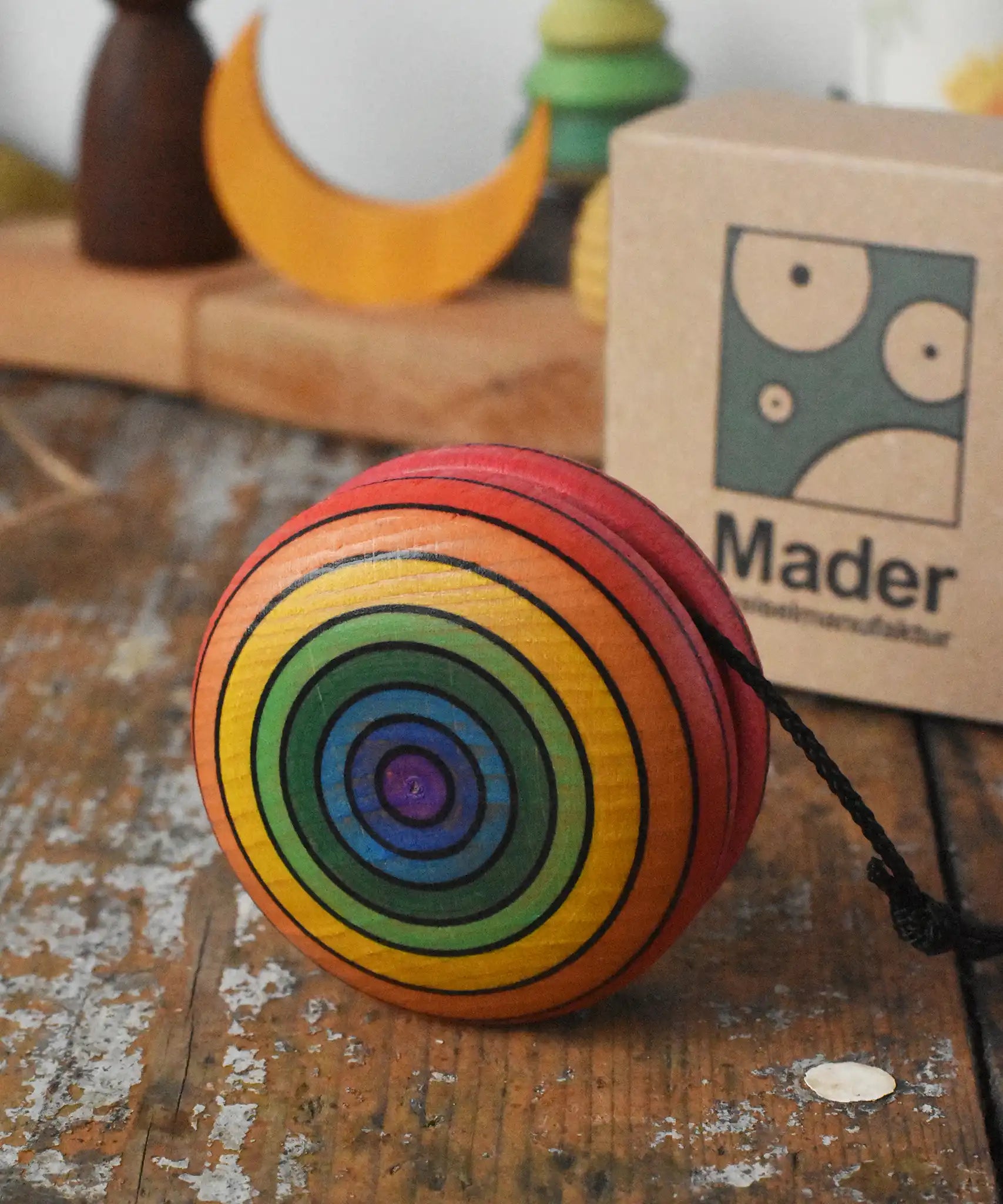Mader yoyo rainbow placed on a wooden desk in the Babipur playroom. Cardboard packaging box can be seen in the background.