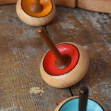 Three Mader Zwirbel Spinning Tops in yellow red and blue placed on a wooden desk in the Babipur playroom.