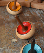 Three Mader Zwirbel Spinning Tops in yellow red and blue placed on a wooden desk in the Babipur playroom.
