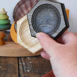 Mader hexagon 8cm spinning top plates in black oak and oak in an adult's hand.