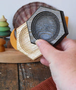 Mader hexagon 8cm spinning top plates in black oak and oak in an adult's hand.