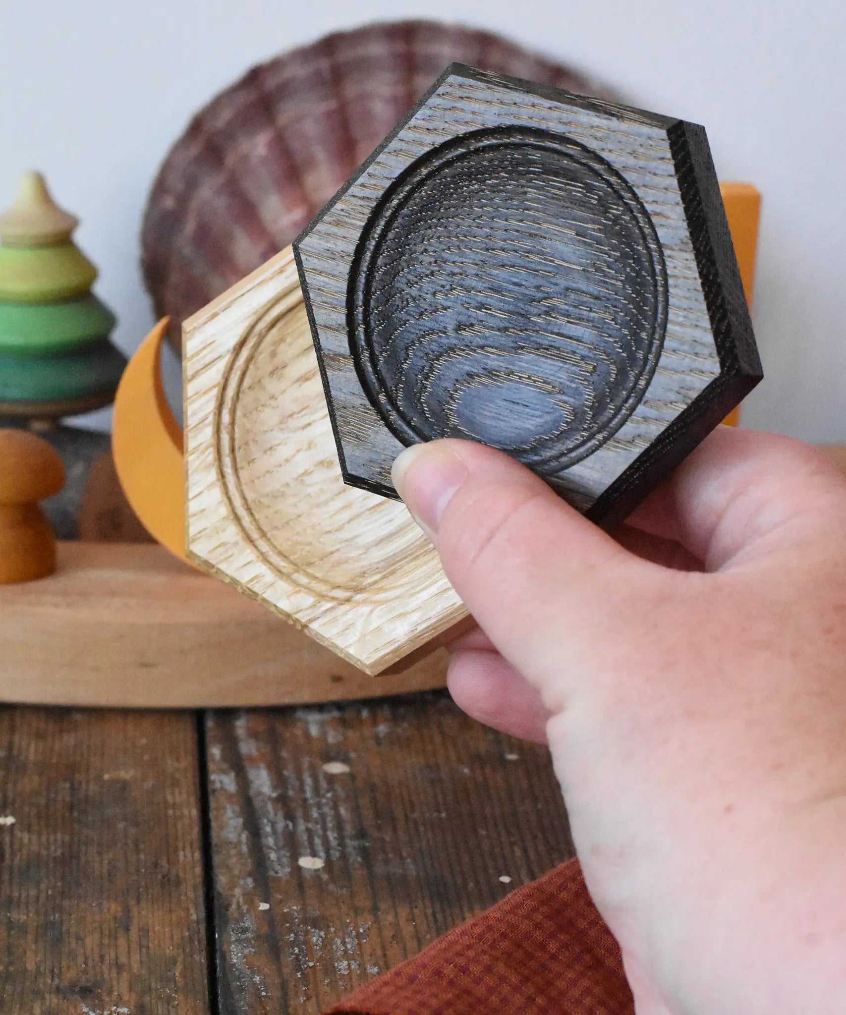 Mader hexagon 8cm spinning top plates in black oak and oak in an adult's hand.