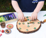 Child placing marbles and mandala pieces on a log slice from the Magic Wood Eco Blocks Big Box 70 piece set, decorating an imaginary pizza.