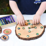 Child placing marbles and mandala pieces on a log slice from the Magic Wood Eco Blocks Big Box 70 piece set, decorating an imaginary pizza.