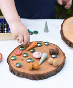Child placing flat glass marbles and Grapat mandala pieces on a large log slice from the Magic Wood Eco Blocks Big Box 70 piece set.