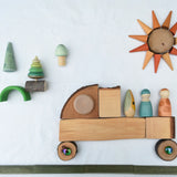 Flat lay created using the Magic Wood Eco Blocks Big Box 70 piece set. A truck with Nins on the back traveling on a green Kapla road with a forest in the background and a sun in the sky.