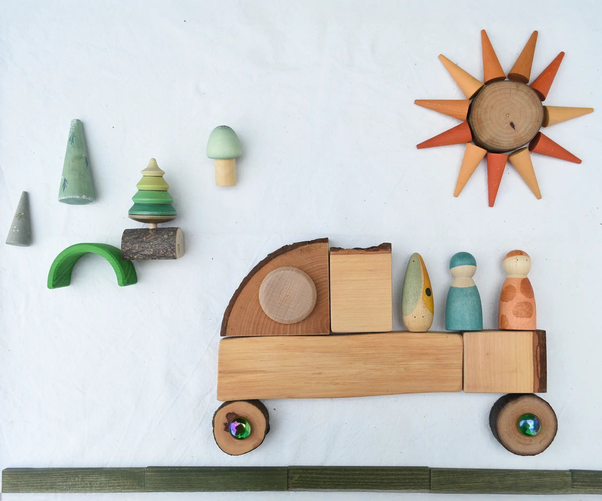 Flat lay created using the Magic Wood Eco Blocks Big Box 70 piece set. A truck with Nins on the back traveling on a green Kapla road with a forest in the background and a sun in the sky.