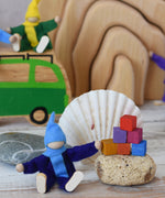 One of the elves from the Magic Wood Six Felt Elves placed in a seated position next to a stone with Grapat Mis and Match cubes stacked on top.