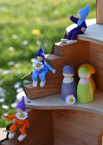 The Magic Wood Six Felt Elves on a tree house with Grimm's friends peg dolls. Some of the elves are holding daisies.  