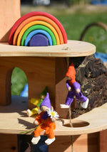 The Magic Wood Six Felt Elves shown with a Magic Wood tree house. One elf is in a seated position holding a daisy.