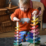 A child kneeling behind the mini and small Magic Wood rainbow marble trees placing wooden and glass marbles on the top rungs. 