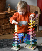 A child kneeling behind the mini and small Magic Wood rainbow marble trees placing wooden and glass marbles on the top rungs. 