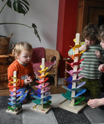 Children sitting around mini, small and large Magic Wood marble trees, placing marbles on the rainbow coloured leaves.