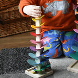 Child with his hand holding the top of the mini Magic Wood wooden rainbow ball run. The wooden marbles are on the square base at the bottom. 