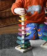 Child with his hand holding the top of the mini Magic Wood wooden rainbow ball run. The wooden marbles are on the square base at the bottom. 