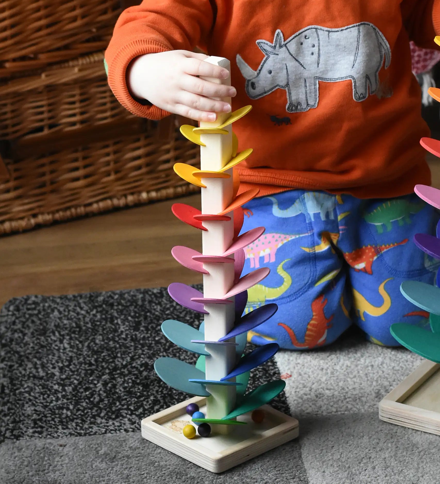 Child with his hand holding the top of the mini Magic Wood wooden rainbow ball run. The wooden marbles are on the square base at the bottom. 