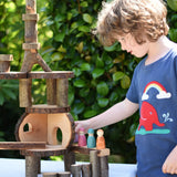 Magic Wood oiled ecoBlocks in a 36 piece set used to build a structure with a child wearing a Babipur t-shirt placing wooden peg dolls on it. 