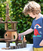 Magic Wood oiled ecoBlocks in a 36 piece set used to build a structure with a child wearing a Babipur t-shirt placing wooden peg dolls on it. 