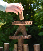 Child's hand placing a tall log piece on the top of a structure created using the Magic Wood oiled ecoBlocks 36 piece set.