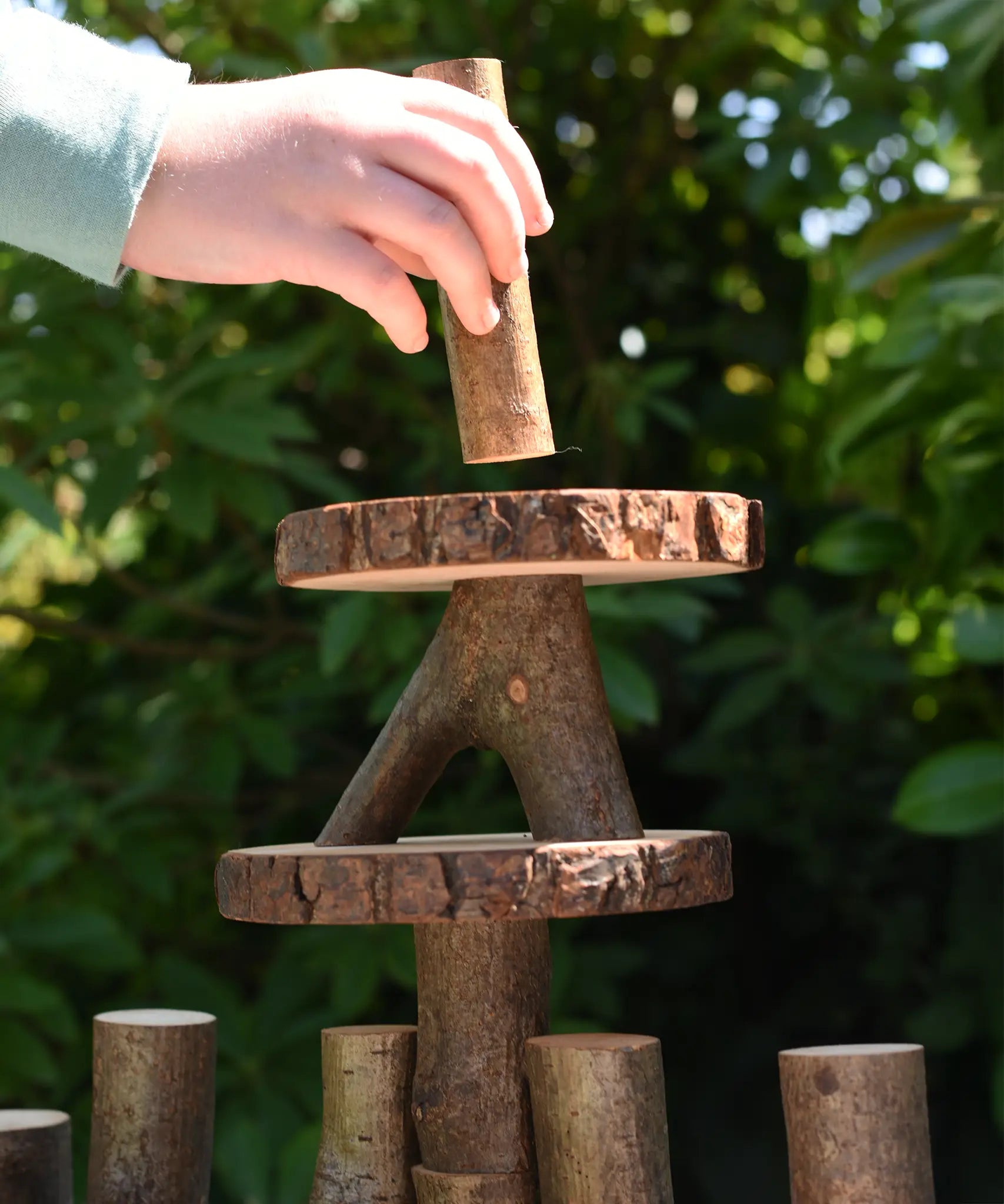 Child's hand placing a tall log piece on the top of a structure created using the Magic Wood oiled ecoBlocks 36 piece set.