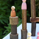 Pieces from the  Magic Wood oiled ecoBlocks 36 piece set stacked up with wooden peg dolls placed on top.