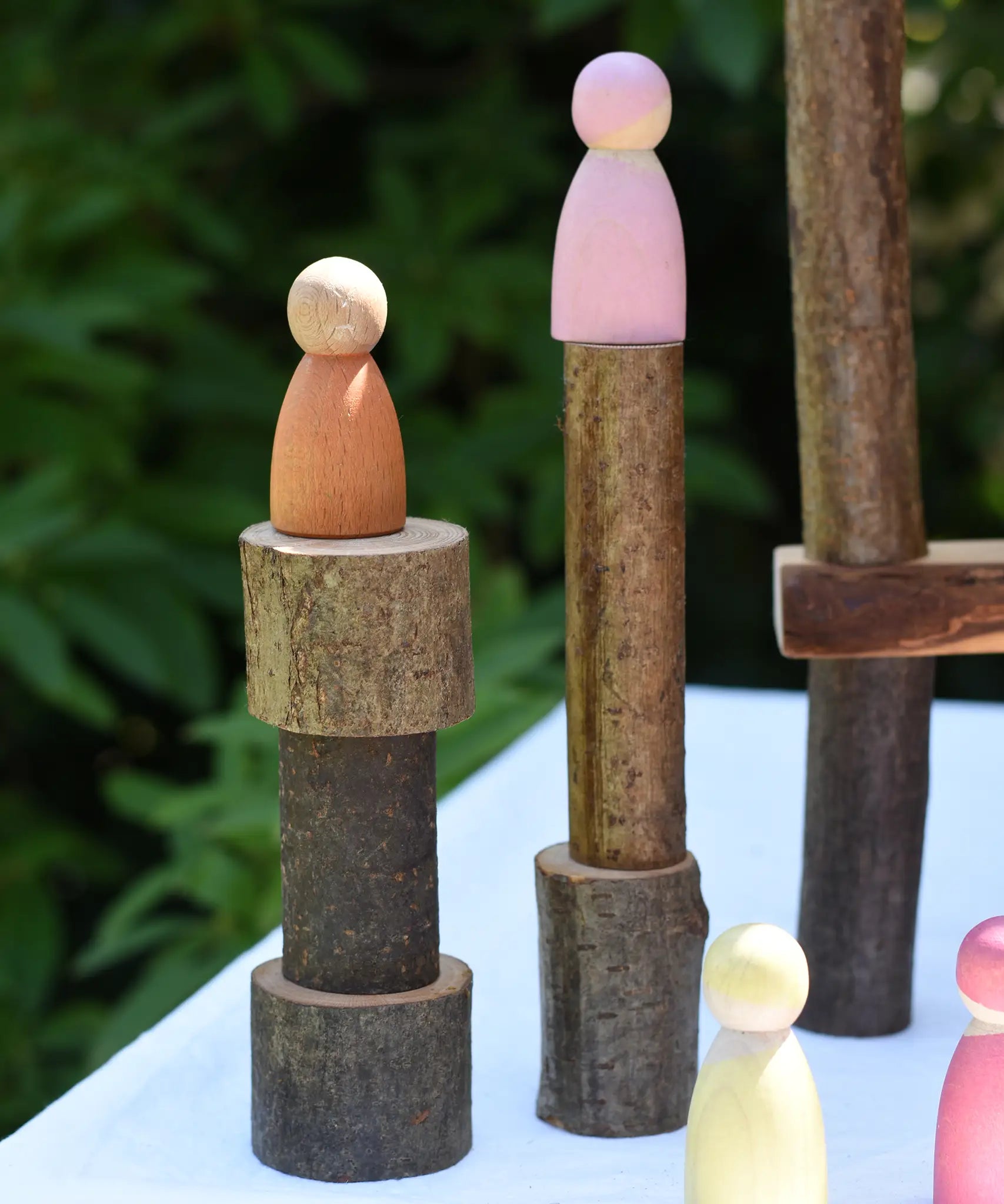 Pieces from the  Magic Wood oiled ecoBlocks 36 piece set stacked up with wooden peg dolls placed on top.