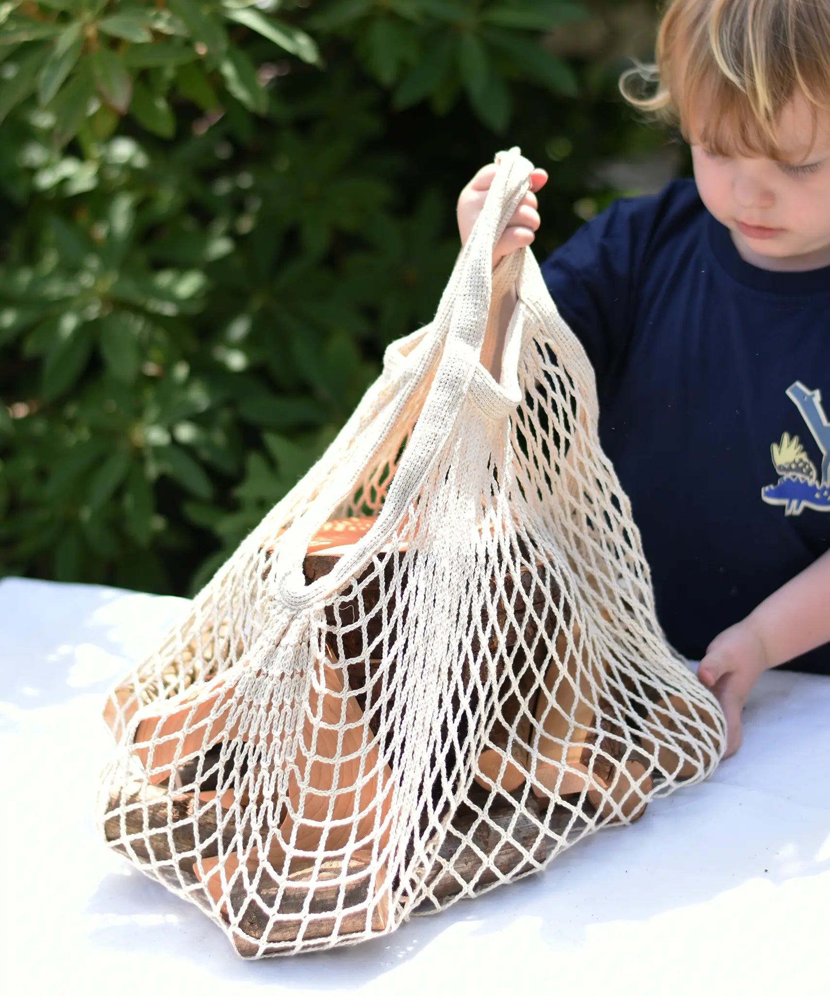Child lifting the net bag containing Magic Wood oiled ecoBlocks in a 36 piece set.