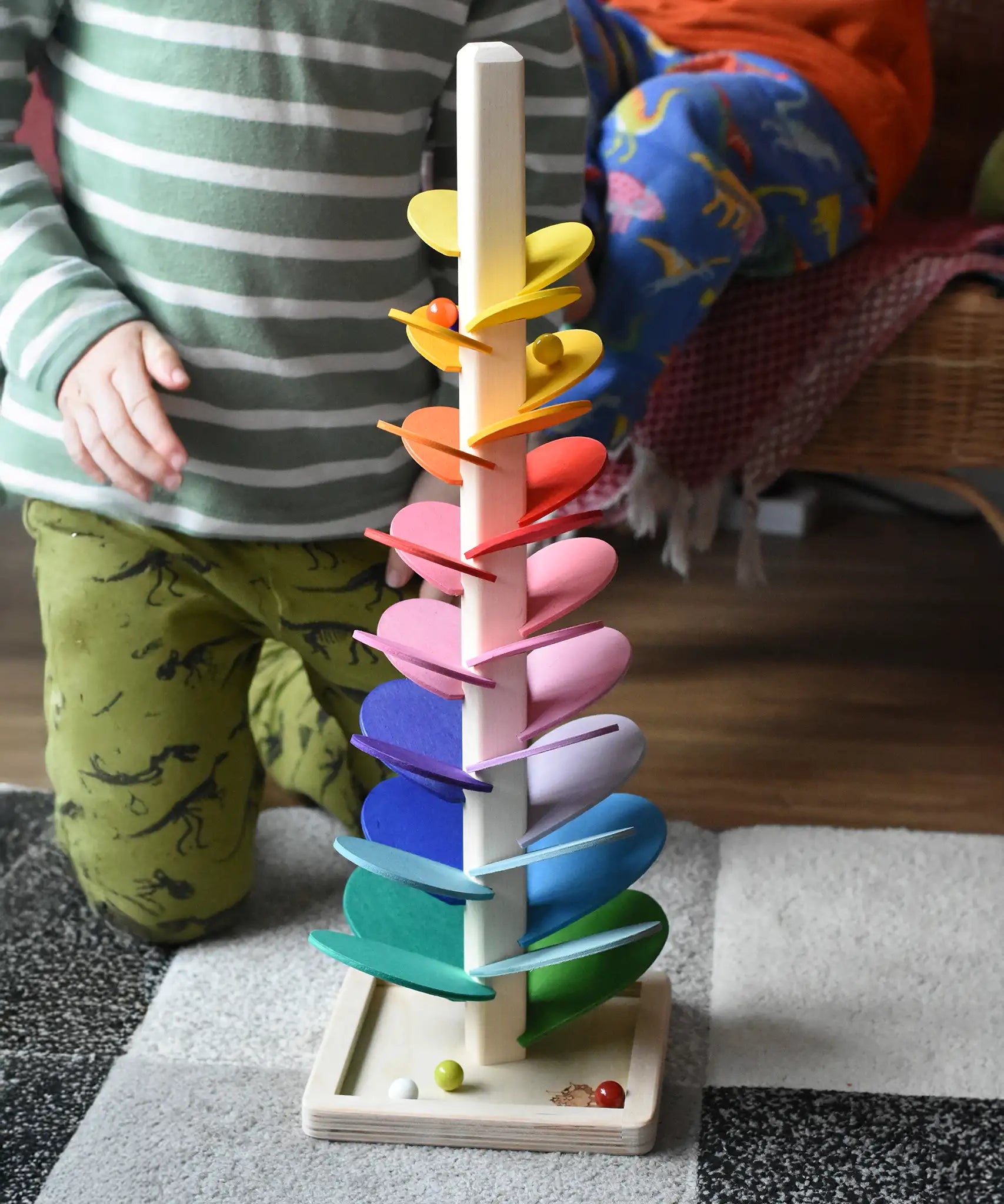 The small Magic Wood rainbow marble tree with glass marble cascading down the wooden leaves. A child kneeling behind.