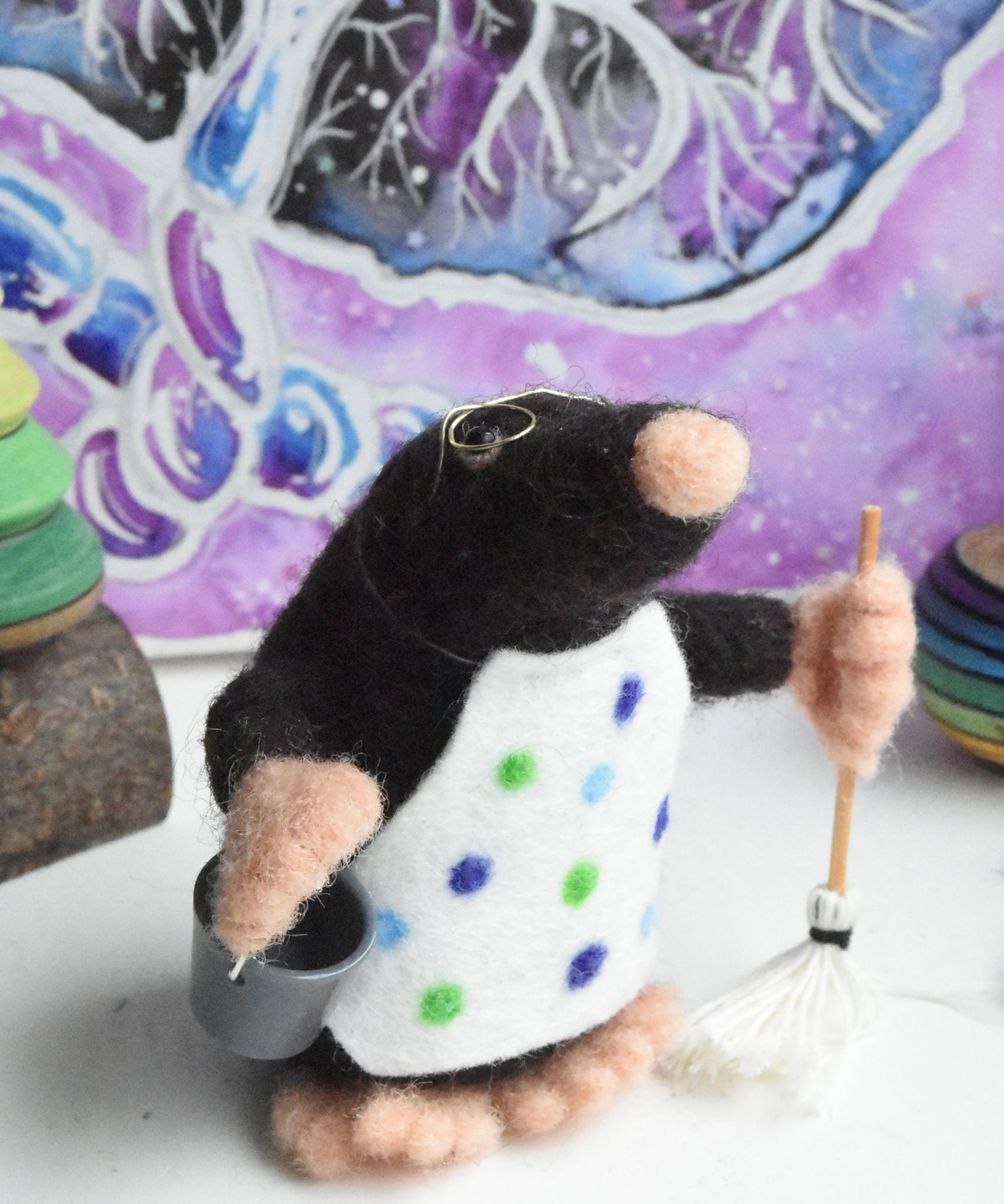 A felted mole figure wearing a spotty apron holding a bucket and a mop. The figure has been created using The Makerss Small Busy Mr Mole Needle Felt Kit.
