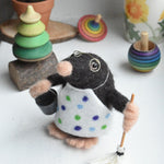 A felted mole figure wearing a spotty apron holding a bucket and a mop. The figure has been created using The Makerss Small Busy Mr Mole Needle Felt Kit.