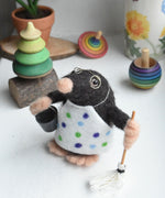 A felted mole figure wearing a spotty apron holding a bucket and a mop. The figure has been created using The Makerss Small Busy Mr Mole Needle Felt Kit.