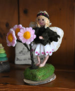 A Daisy flower fairy placed on a wooden dresser. The fairy has been made using The Makerss Official Flower Fairies Daisy Fairy Needle Felt Kit.