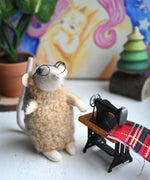 A little mouse figure standing my a mini sewing machine. The figure has been handmade using The Makerss Small Sewing Mouse Needle Felt Kit