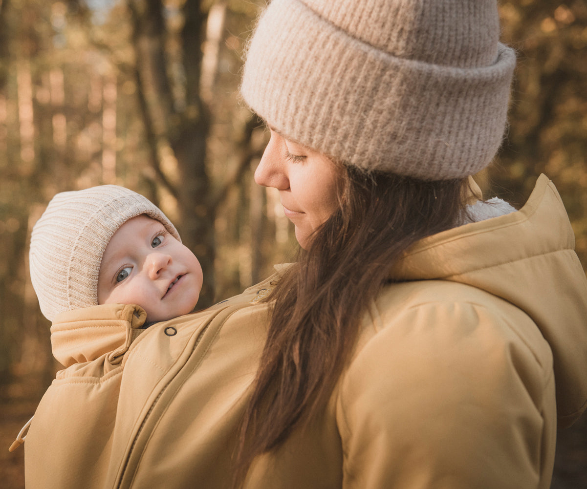 A close up of a woman and baby wearing the Mamalila Allweather Cosy Allrounder Babywearing Jacket in a Mustard yellow colour.
