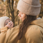 A close up of a woman and baby wearing the Mamalila Allweather Cosy Allrounder Babywearing Jacket in a Mustard yellow colour.