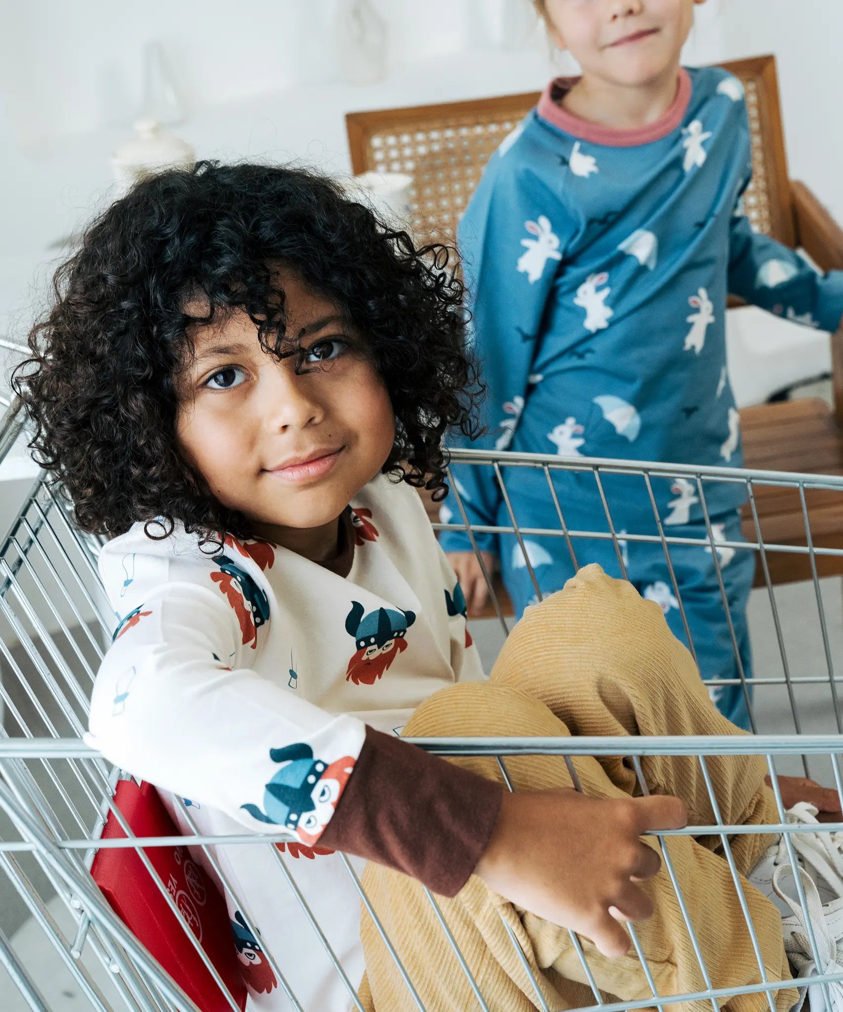 Child sitting in a trolley wearing the Maxomorra organic cotton long sleeved viking print top with mustard yellow trousers. 