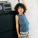 Child wearing the Maxomorra kids GOTS organic cotton boxer shorts in a blue, white, yellow and brown striped design with a blue vest top.