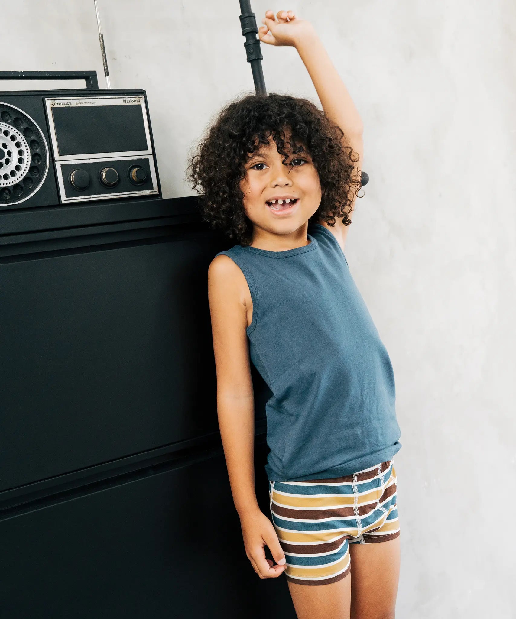 Child wearing the Maxomorra kids GOTS organic cotton boxer shorts in a blue, white, yellow and brown striped design with a blue vest top.