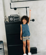 Child wearing the Maxomorra kids GOTS organic cotton boxer shorts in a blue, white, yellow and brown striped design with a blue vest top.