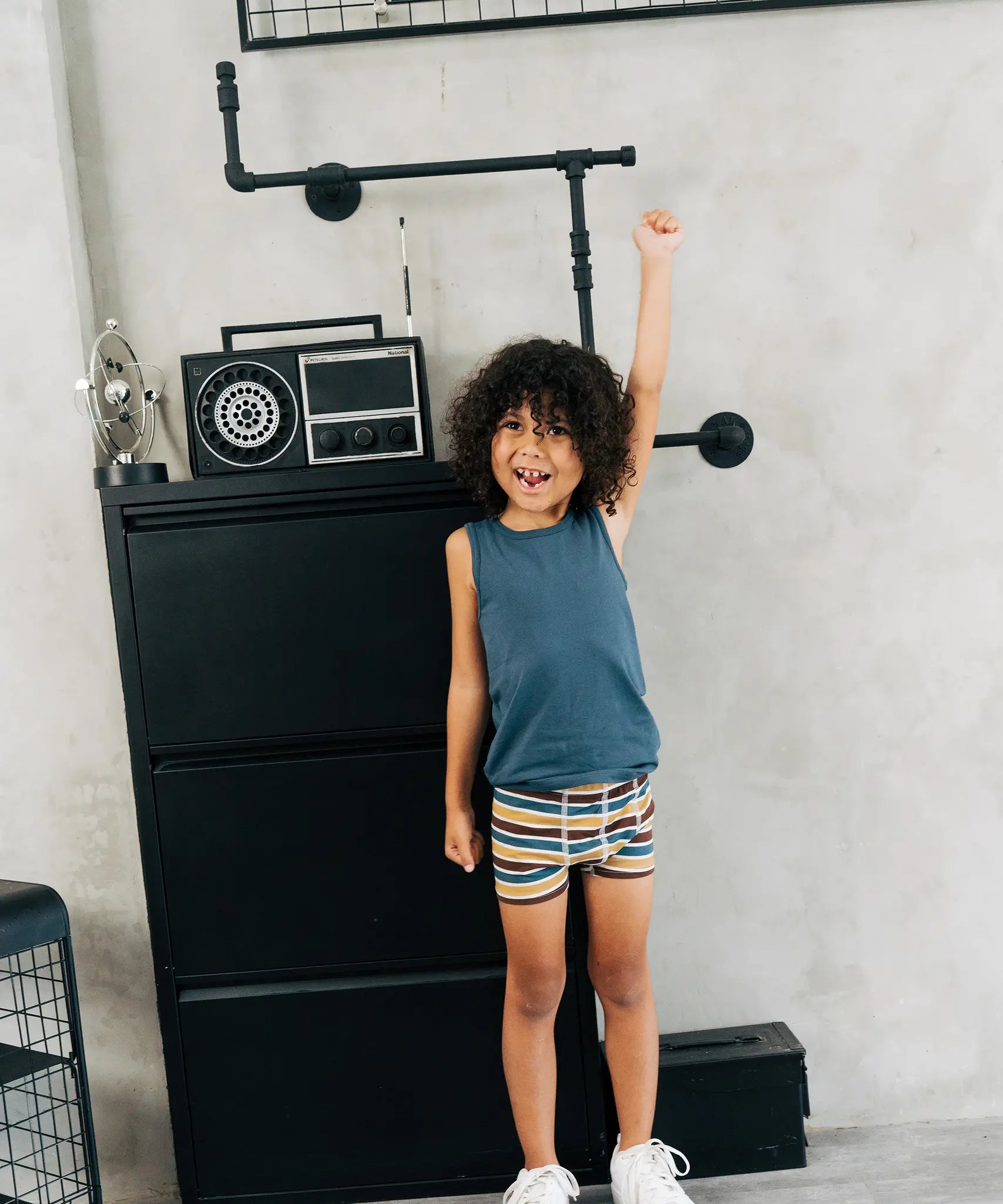 Child wearing the Maxomorra kids GOTS organic cotton boxer shorts in a blue, white, yellow and brown striped design with a blue vest top.