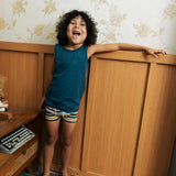 Child wearing the Maxomorra kids GOTS organic cotton boxer shorts in a blue, white, yellow and brown striped design with a blue vest top.