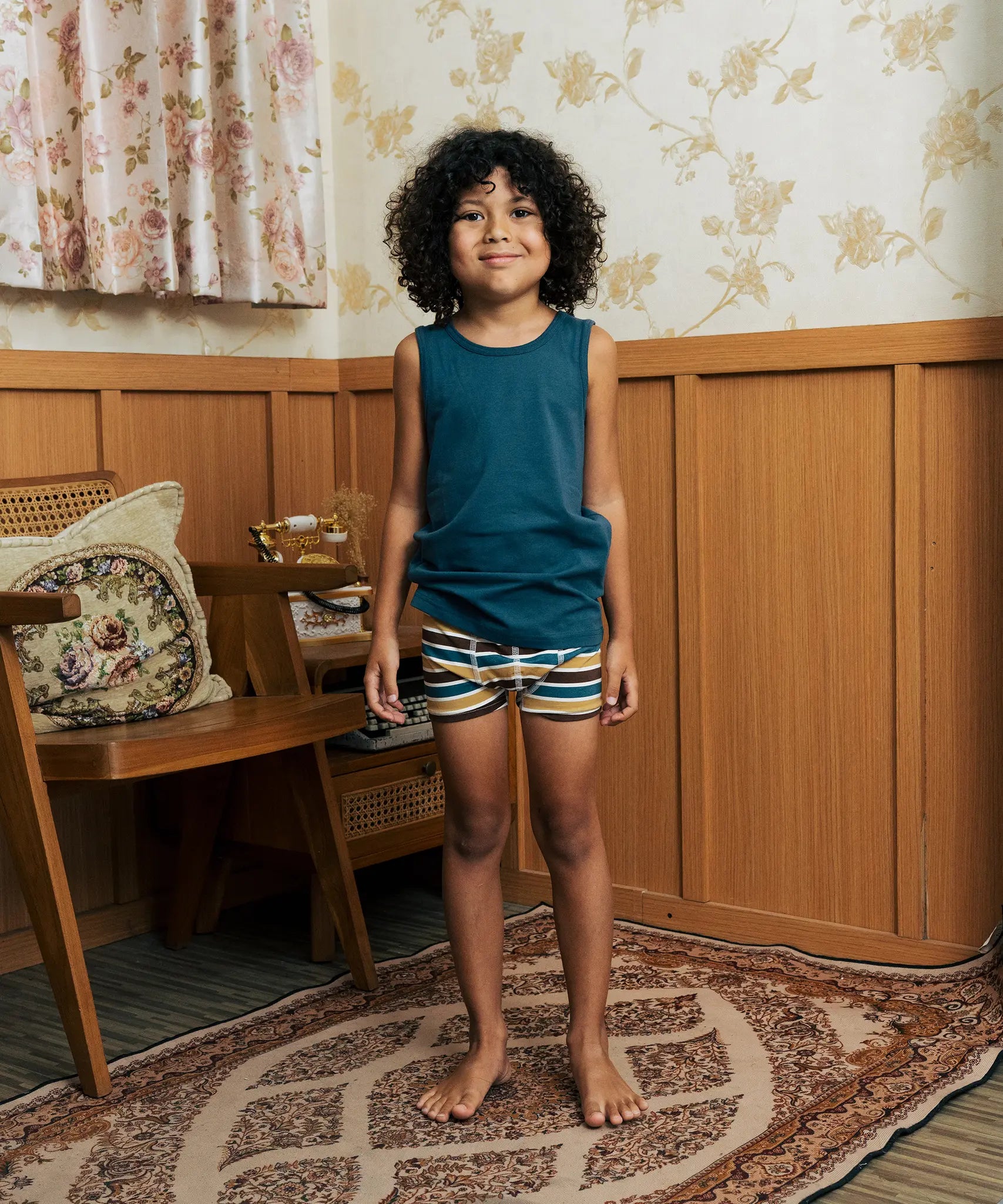 Child wearing the Maxomorra kids GOTS organic cotton boxer shorts in a blue, white, yellow and brown striped design with a blue vest top.