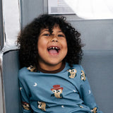 Child smiling wearing the Maxomorra GOTS organic cotton long sleeve top in blue with a cute repeating owl print and brown neck line and cuffs.