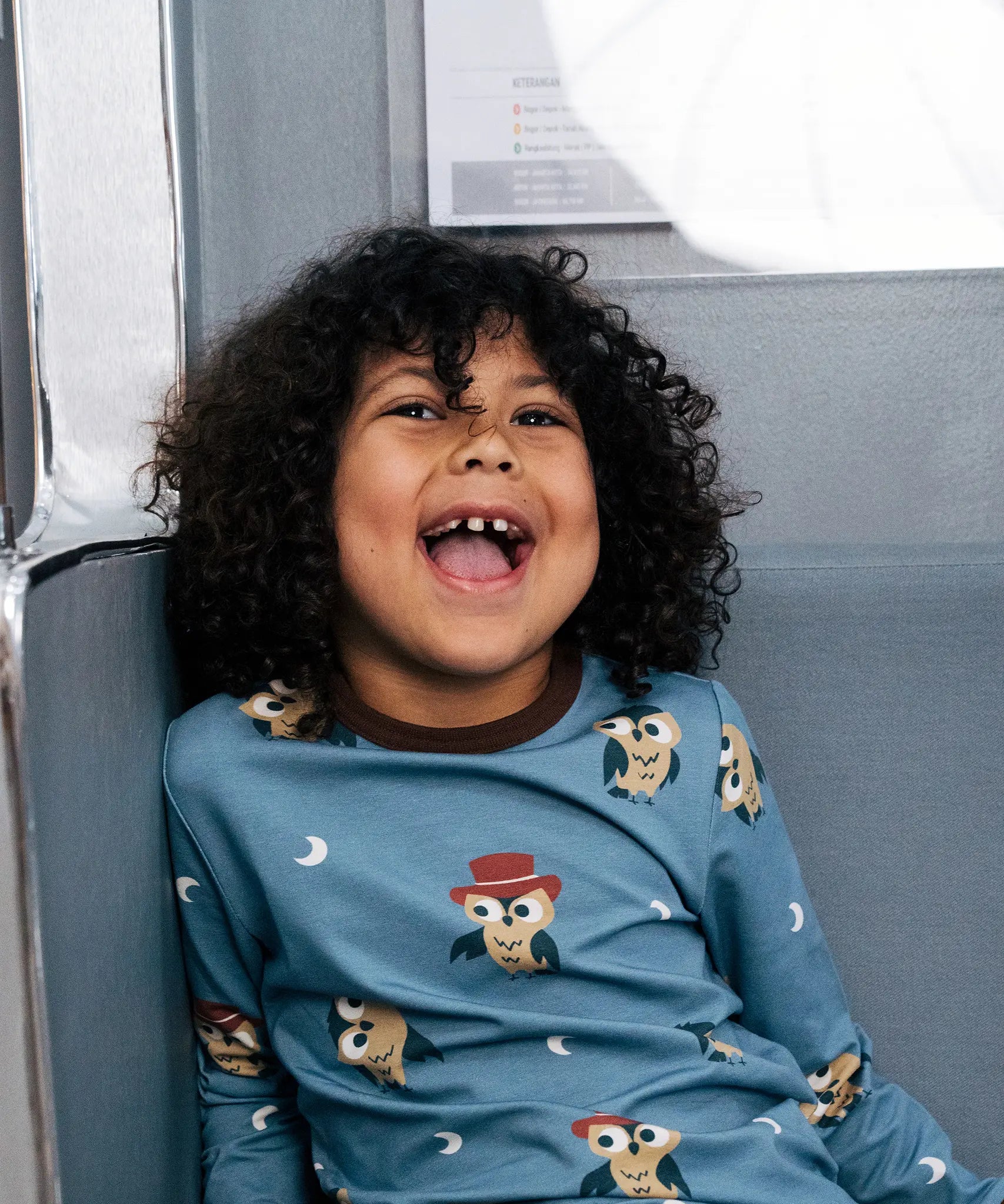 Child smiling wearing the Maxomorra GOTS organic cotton long sleeve top in blue with a cute repeating owl print and brown neck line and cuffs.