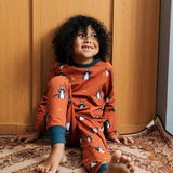 Child wearing the Maxomorra kids dragons organic cotton long sleeve top with pyjama trousers. Red top with repeat blue dragon print and blue arm cuffs and binding on the neck. 
