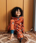 Child wearing the Maxomorra kids dragons organic cotton long sleeve top with pyjama trousers. Red top with repeat blue dragon print and blue arm cuffs and binding on the neck. 
