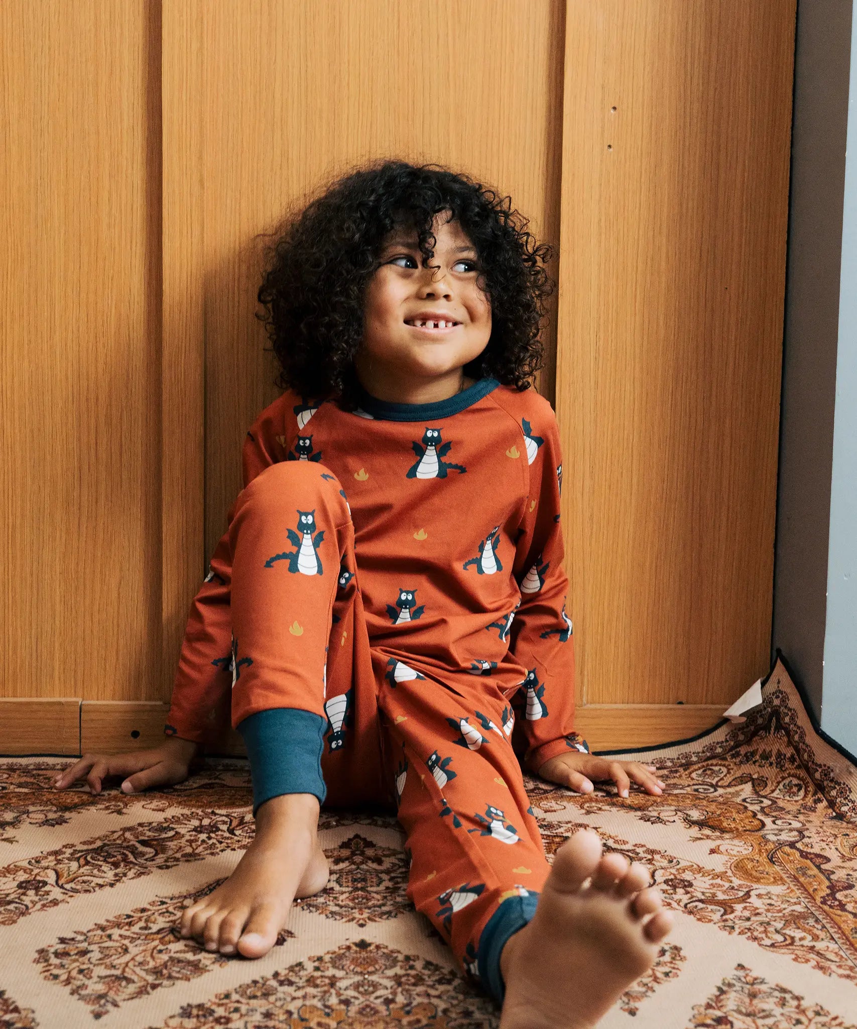 Child wearing the Maxomorra kids dragons organic cotton long sleeve top with pyjama trousers. Red top with repeat blue dragon print and blue arm cuffs and binding on the neck. 
