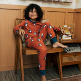 Child wearing the Maxomorra kids dragons organic cotton long sleeve top with pyjama trousers. Red top with repeat blue dragon print and blue arm cuffs and binding on the neck. 
